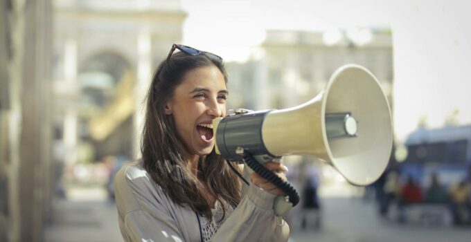 Cheerful young woman screaming into megaphone