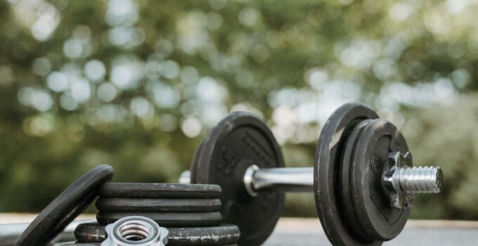 Ground level of adjustable dumbbell on stainless steel bar near plates and screw collars on rough walkway on street