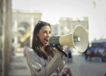 Cheerful young woman screaming into megaphone