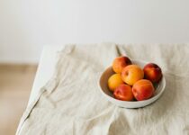 Bunch of ripe apricots in bowl placed on creasy tablecloth on white table