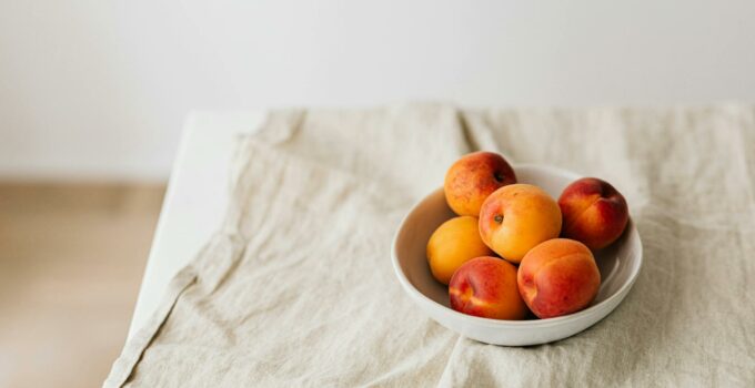 Bunch of ripe apricots in bowl placed on creasy tablecloth on white table