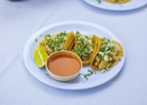A plate of tacos with sauce and a cup of salsa