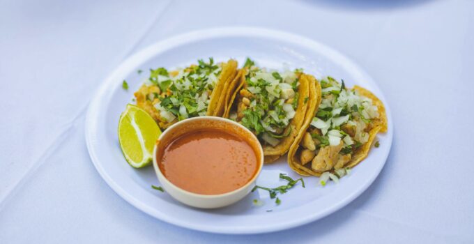 A plate of tacos with sauce and a cup of salsa