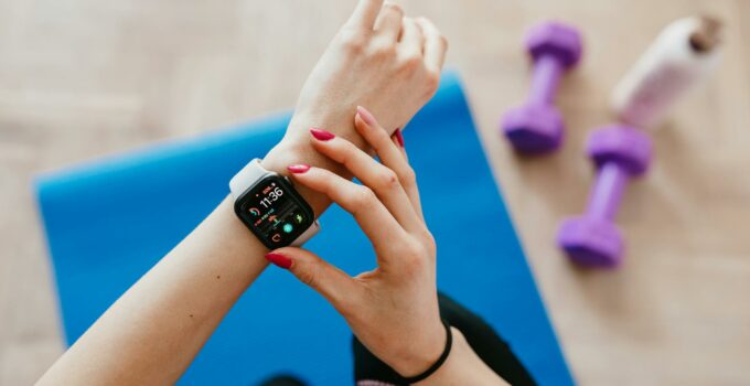 Anonymous sportswoman checking smart watch and sitting on mat