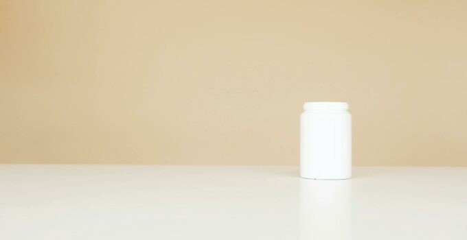 White plastic pills bottle left open on white table against light brown background