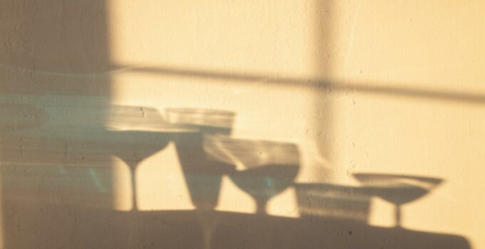 Shadows of different crystal glasses filled with drinks reflecting on white wall in sunlight