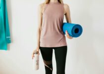 Faceless slim female athlete in sportswear standing with blue fitness mat and water bottle while preparing for indoors workout