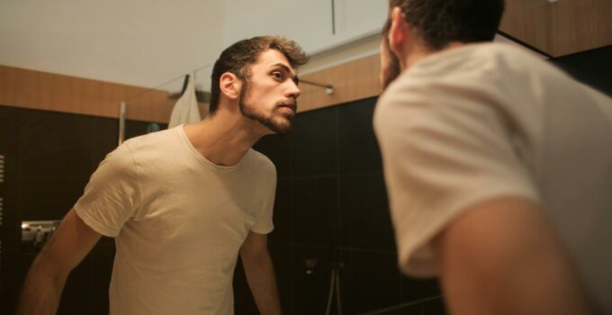 Stylish concentrated man looking in mirror in bathroom