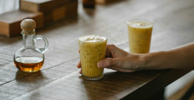 Crop anonymous person sitting at wooden table in modern restaurant and holding glass with fresh healthy smoothie