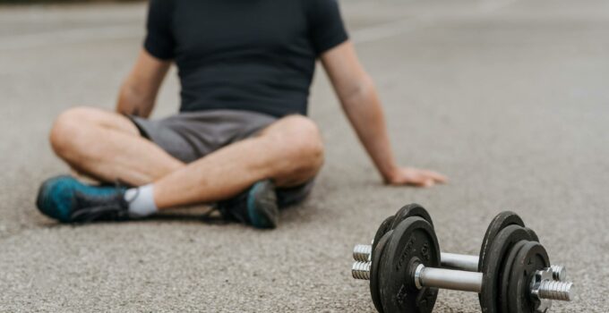 Crop sportsman resting on road near dumbbells after working out