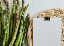 Top view of asparagus pods with sheets of paper fastened by paper clip on white desktop