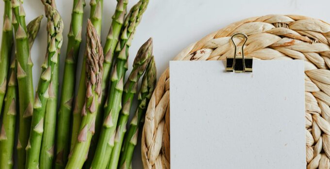 Top view of asparagus pods with sheets of paper fastened by paper clip on white desktop