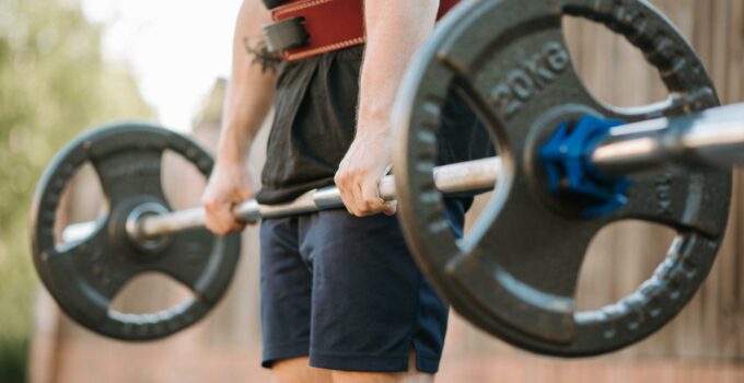 Crop anonymous sportsman in weight belt lifting heavy barbell during training near wall in town