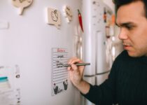 Young man writing reminder on fridge note